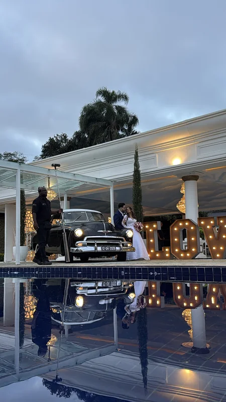 Chevrolet 1951 preto estacionado ao lado de espelho d'água e letreiro LOVE iluminado em espaço de eventos