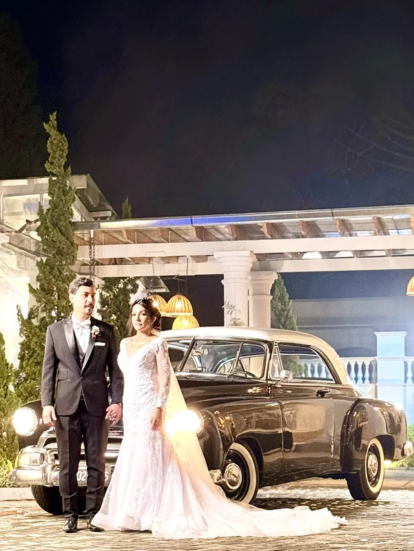 Lateral do Chevrolet 1951 preto com noivo de terno e noiva de vestido sereia em frente a um pergolado