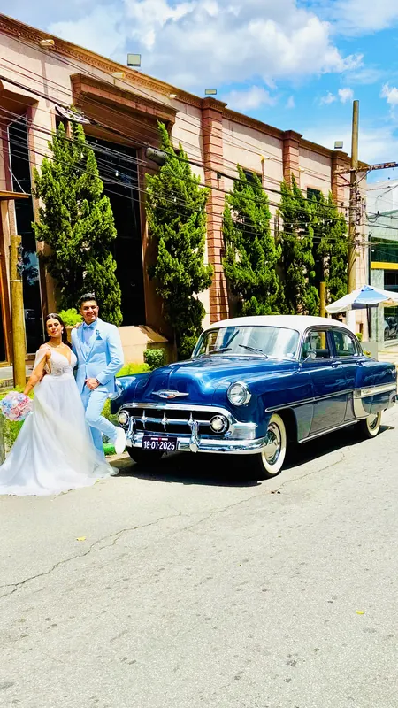 Bel Air 1953 azul estacionado em rua com casal de noivos de azul-claro em frente a prédio histórico