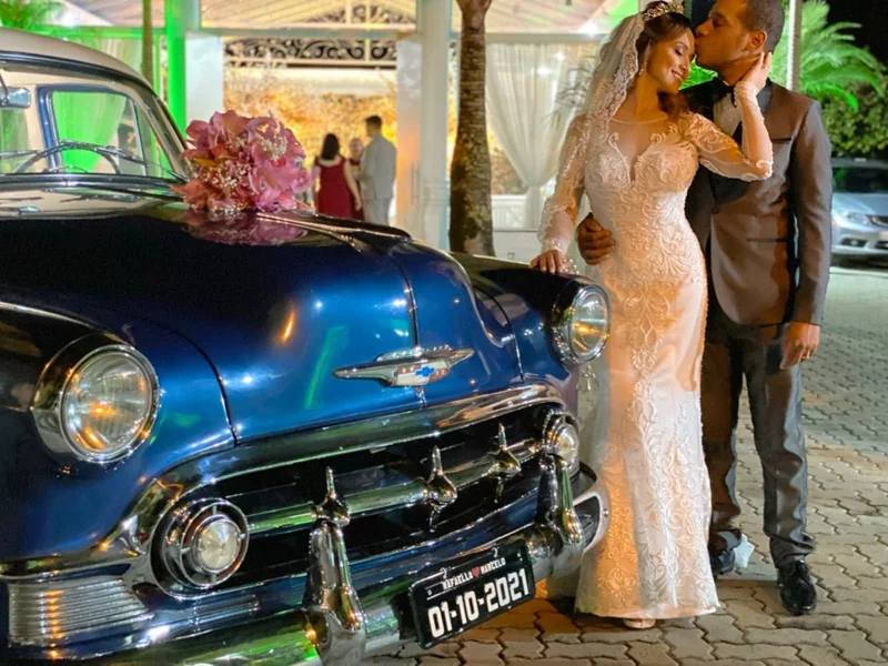 Farol, grade cromada e placa do Bel Air 1953 azul com noiva e noivo atrás