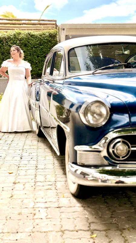Frente e lateral do Chevrolet Bel Air 1953 azul com pneus de faixa branca, noiva em pé ao fundo