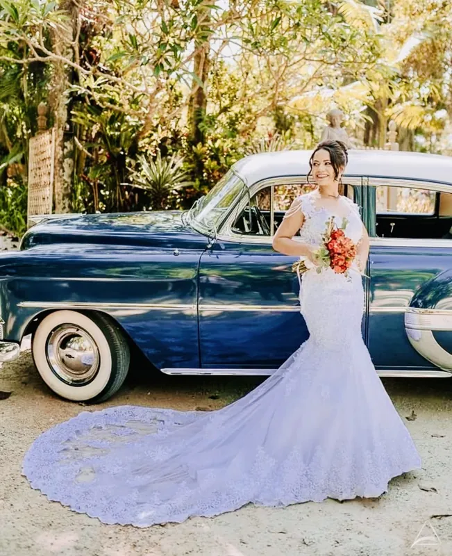 Noiva de vestido sereia com cauda em pé ao lado do Bel Air 1953 azul, pneus de faixa branca à mostra
