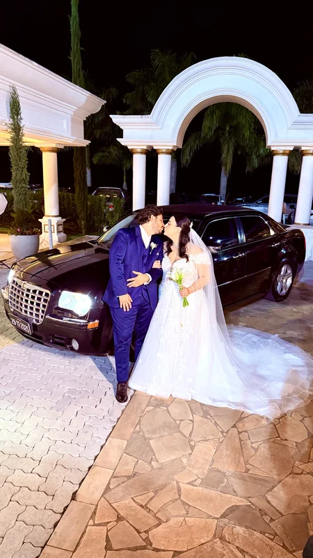 Casal se beijando ao lado do Chrysler 300C preto diante de um arco branco à noite