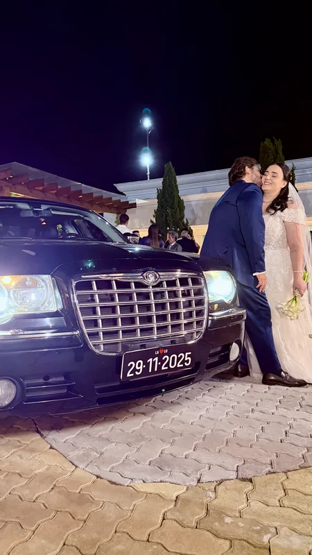Grade cromada e faróis do Chrysler 300C à noite com casal de noivos atrás