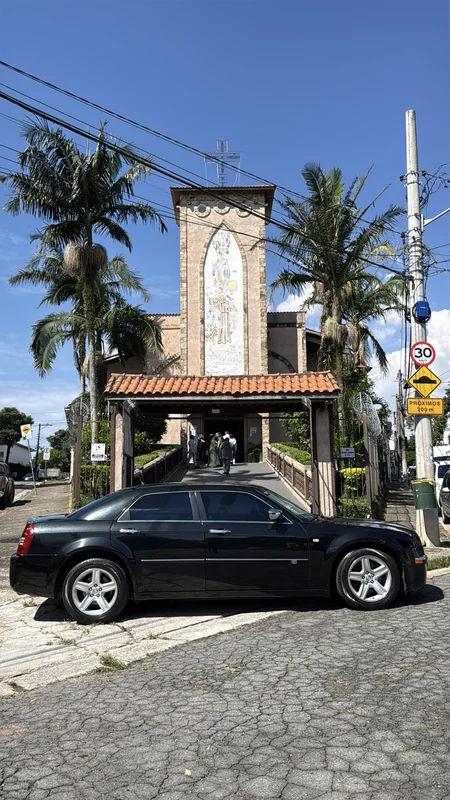 Chrysler 300C preto estacionado em frente a uma capela com palmeiras