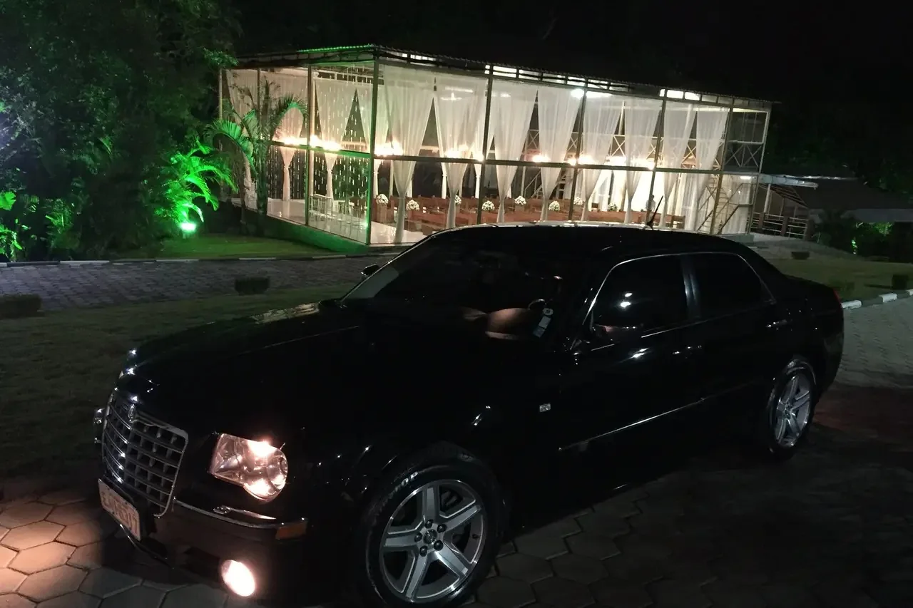 Lateral do Chrysler 300C preto à noite em frente a salão de vidro iluminado