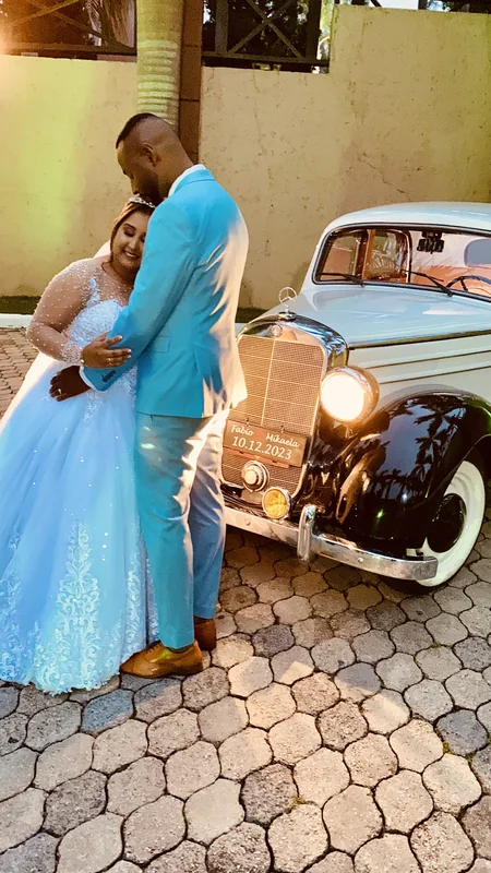 Casal de azul-claro abraçado ao lado do Mercedes-Benz 170S em piso de pedra